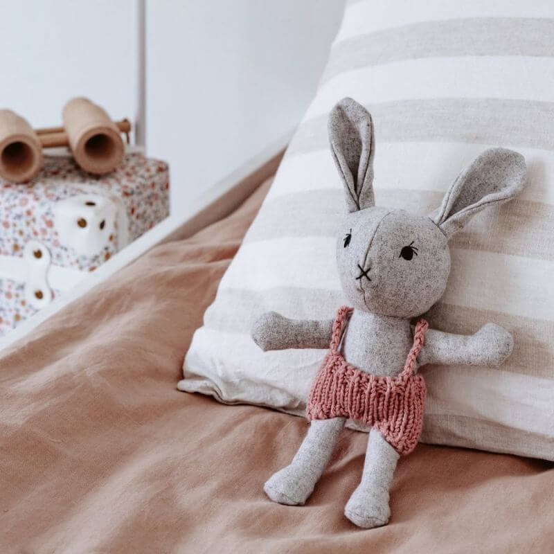 softies mini agatha rabbit in pink overalls and sitting on a bed