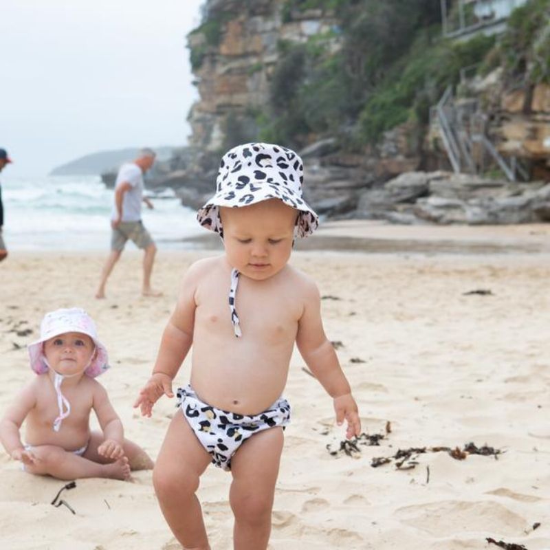 toddler walking on beach with leopard print swim nappy and matching hat