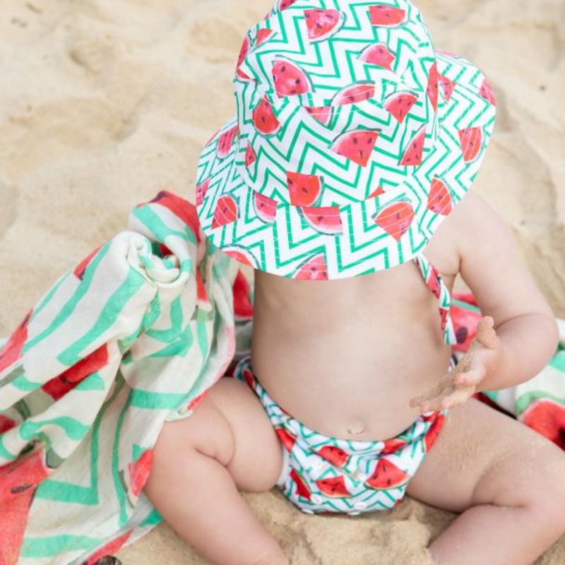 baby sitting on beach with watermelon print swim nappy and matching hat
