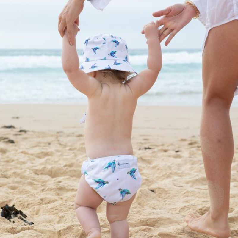 child walking on beach wearing sea turtles swim nappy and hat