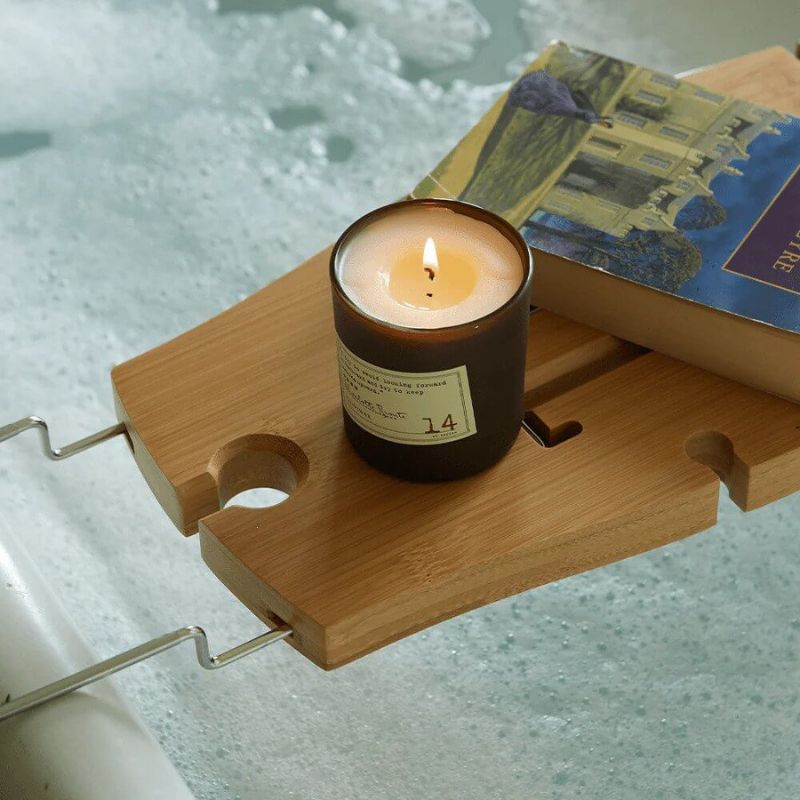a lit paddywax candle on tray over a bubble bath