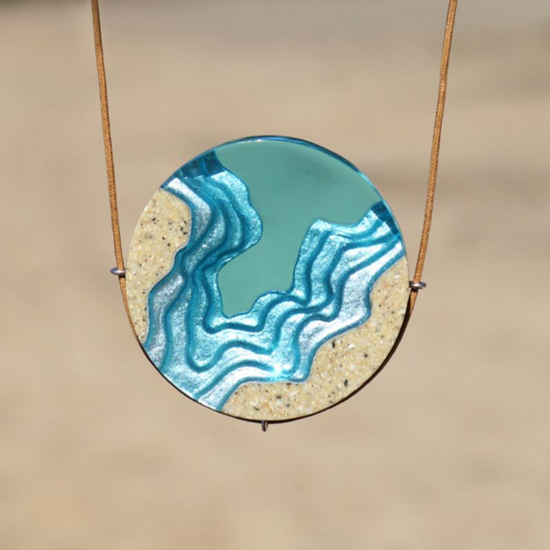 Necklace with a round disc showing a topographical design of an abyss with resin and sand