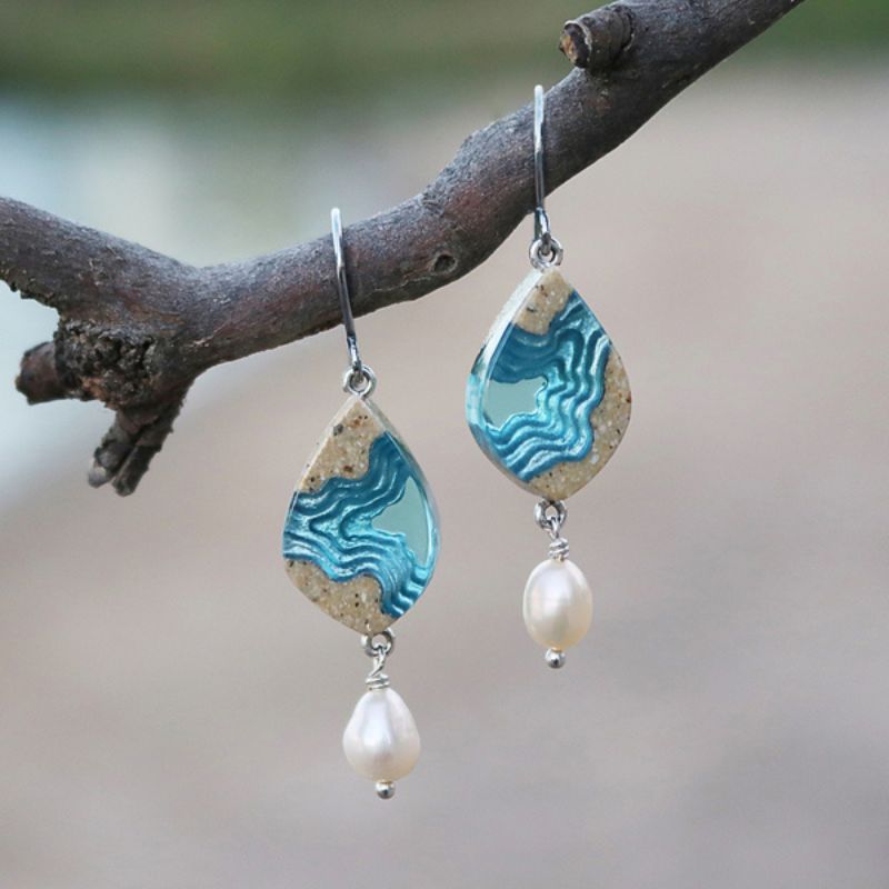 earrings made from resin and sand depicting the topography of a bay with a pearl accent