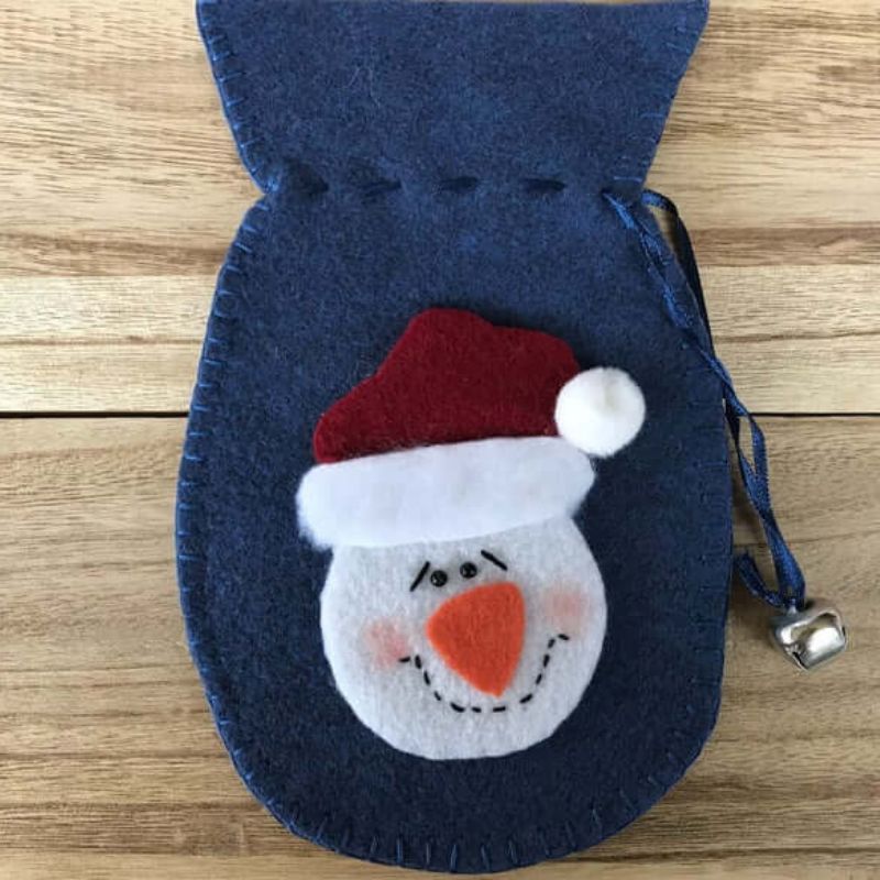 felt decoration ornament in the shape of a mitten with accented bell with a felt snowman and hat on the front