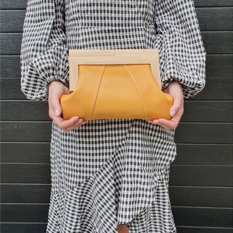 Lady holding a saffron yellow italian leather clutch with wooden handle