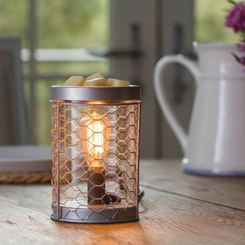 Brown metal electric candle warmer with glass and chicken wire inserts showing an edison bulb