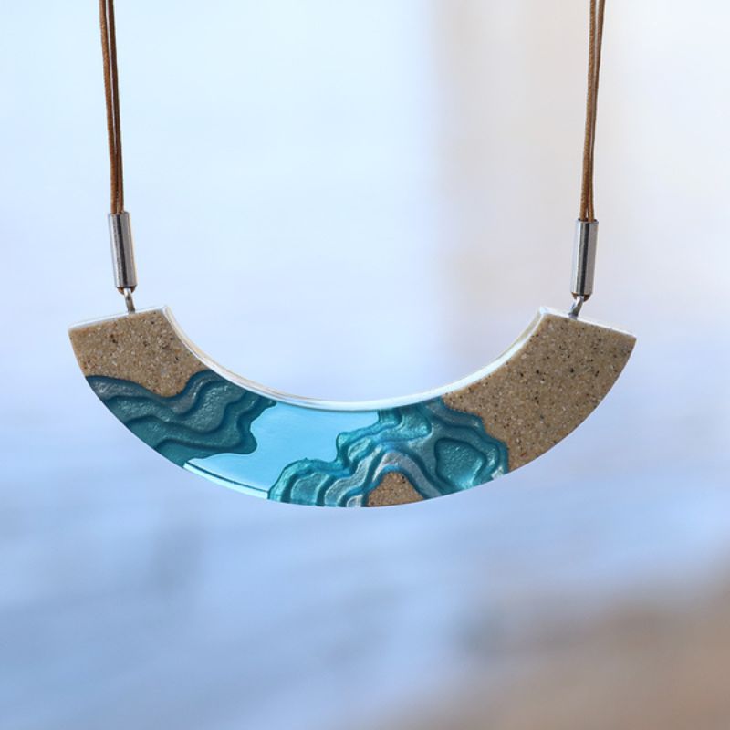 necklace in a half moon design with lagoon topographical design in sand and aqua resin