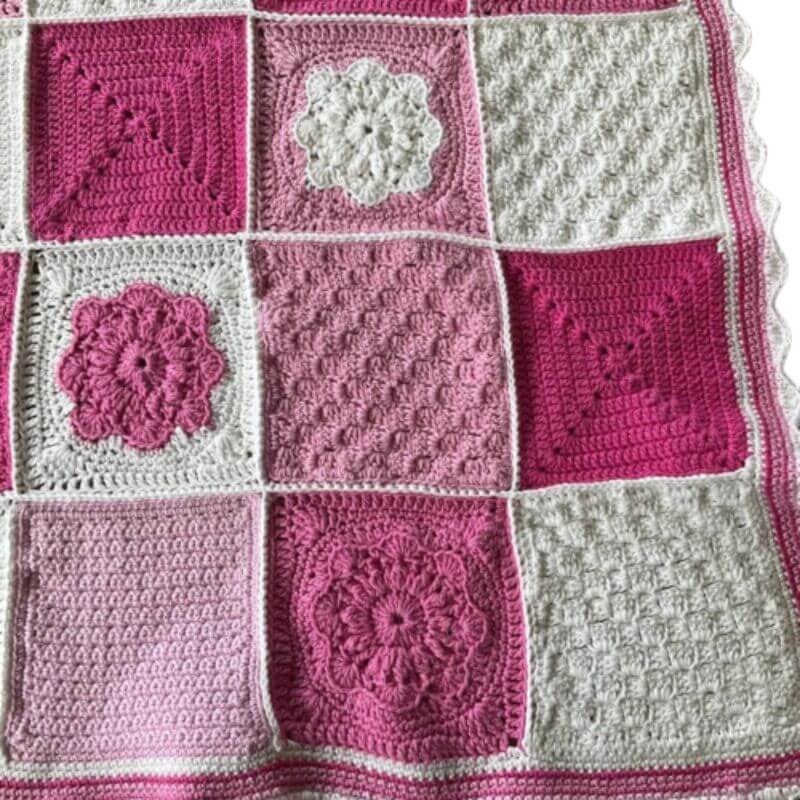 100% cotton cot size baby blanket showing flowers and textured squares in pink and white