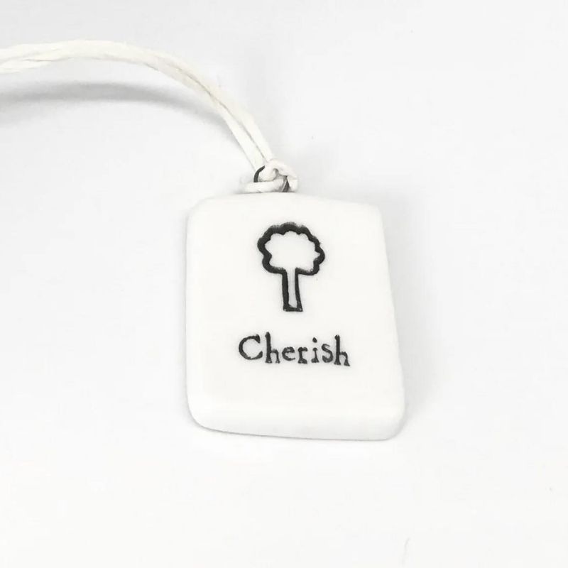 white porcelain tag with a black tree and the word cherish
