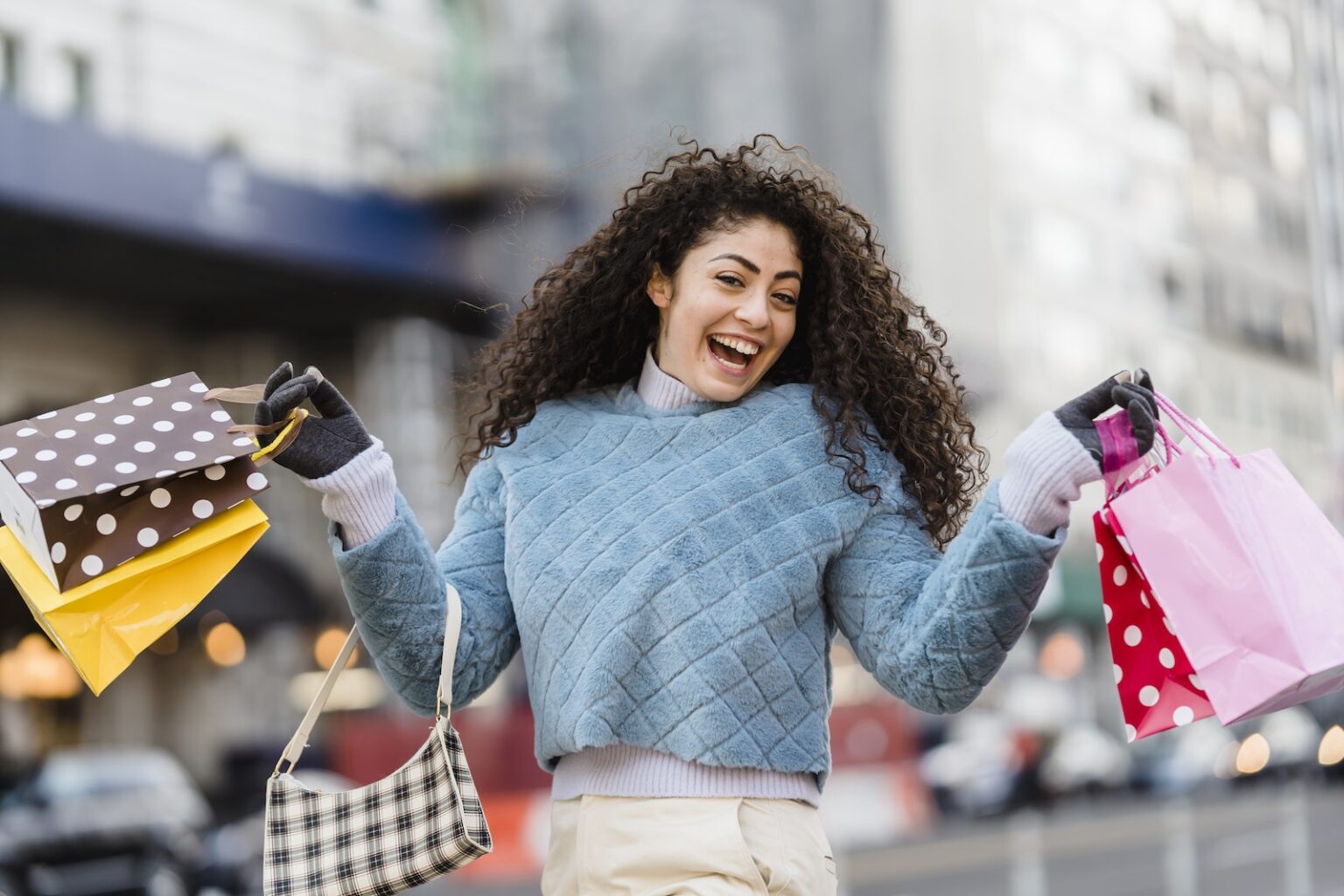 Crop anonymous female in blue soft sweater with many different colorful gift bags on blurred background